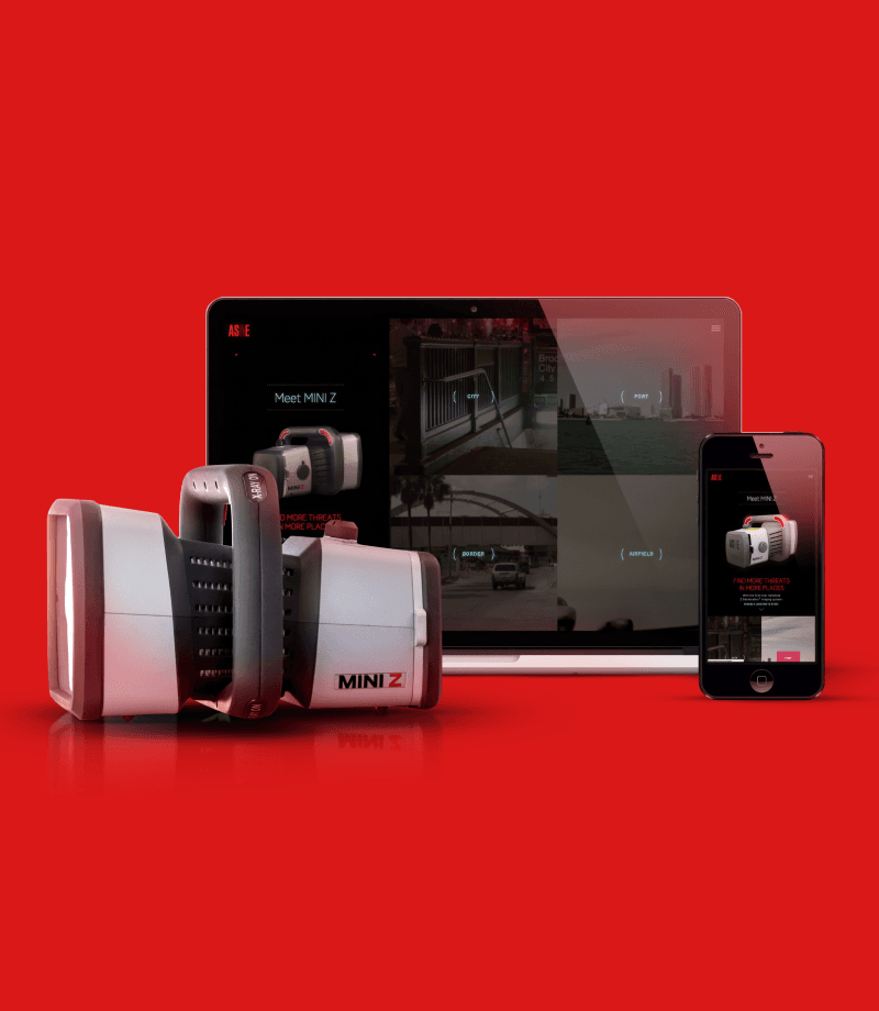 The MINI Z portable scanning device, displayed next to a tablet and a phone. The device is approximately one foot long with a boxy, roughly rectangular shape and an x-ray scanning surface at one end. There is a 2-handed offset handle in the center of its length, with a button marked X-ray On. The tablet and phone each display a 3D model of the device alongside images of four potential use contexts: city, port, border, and airfield.